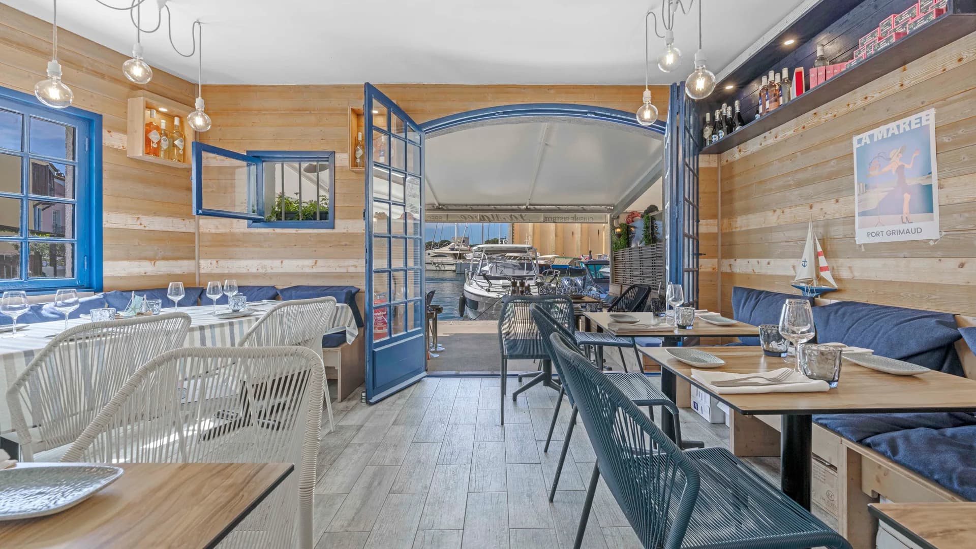 Salle intérieure du restaurant La Marée à Port Grimaud — bois clair, banquettes bleu marine et vue sur les bateaux du port