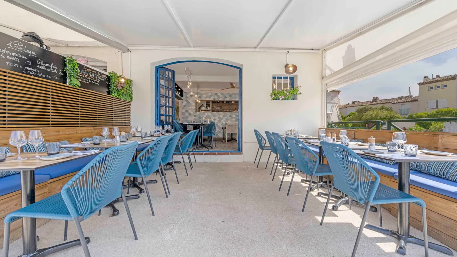 Terrasse couverte du restaurant La Marée à Port Grimaud — chaises bleues, tables dressées et ardoise des suggestions du jour